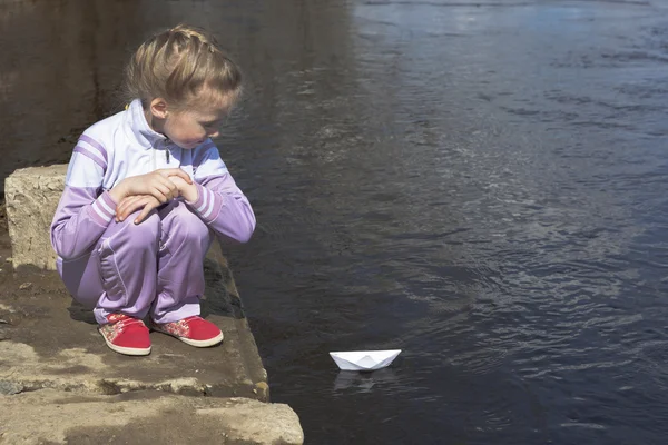 女孩看起来像一艘纸船漂浮在河上 — 图库照片