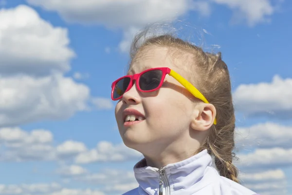 Dromerige klein meisje dragen zonnebril tegen de hemel met wolken kijken naar de top — Stockfoto