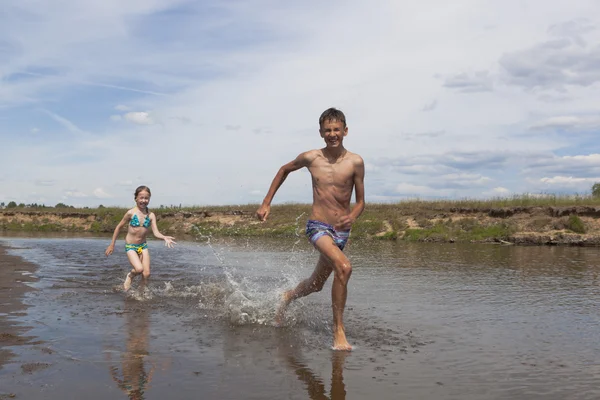 Szczęśliwe dzieci biegną wzdłuż rzeki — Zdjęcie stockowe