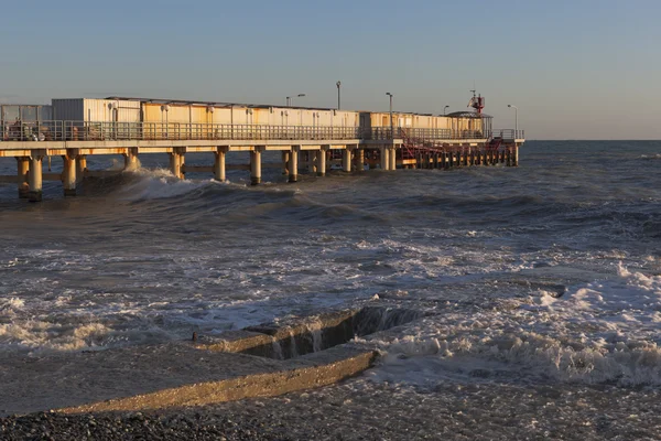 Große Welle bedeckte Wellenbrecher an der Seebrücke in der Feriensiedlung adler in der untergehenden Sonne — Stockfoto