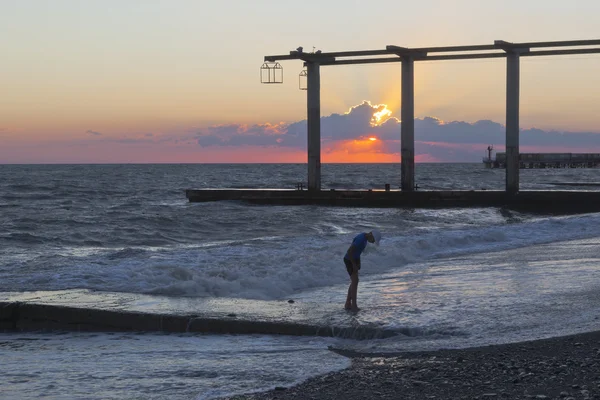 Ragazzo cammina sull'acqua in spiaggia sullo sfondo di un bellissimo tramonto — Foto Stock