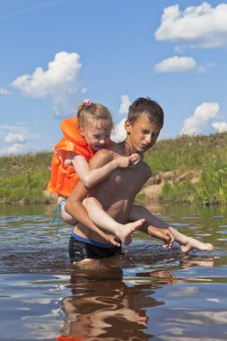 Ciddi çocuk neşeli küçük bir kız nehrin taşır.