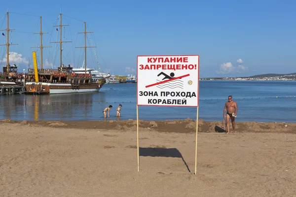 Znak "zakaz kąpieli! Strefa przepływu statków"na tle ludzi kąpieli przy nabrzeżu w Gelendzhik, Krasnodar region, Federacja Rosyjska — Zdjęcie stockowe