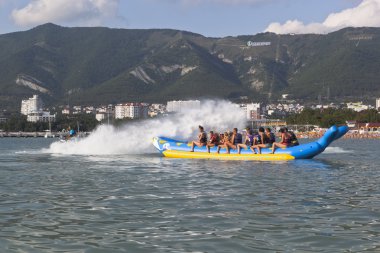 Horseback on an inflatable raft in Gelendzhik Bay. Driver of motorcycle aqueous drenches water attraction participants. Beach resort Gelendzhik, Krasnodar region, Russia
