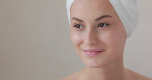 Portret van een mooie jongedame die opzij kijkt terwijl ze poseert op camera met badhanddoek op haar hoofd. Spa behandeling en ochtend routine. Huidverzorgingsconcept. — Stockvideo