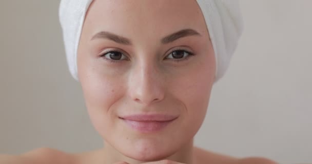 Glimlachende jonge vrouw met zuivere huid gewikkeld in badhanddoek genietend van ochtendprocedures na de douche. Geïsoleerd over witte studio achtergrond. — Stockvideo
