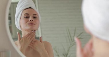 Banyodaki aynaya bakarken cildini yüz kremiyle yumuşatan hoş, genç bir bayan. Evde sabah rutini kavramı.