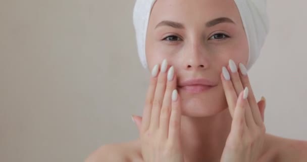 Heureuse jeune femme enveloppée dans une serviette regardant sa peau parfaite après la douche. Jolie femme touchant doucement son visage avec les doigts. Isolé sur fond de studio. — Video