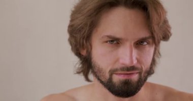 Şık saç kesimli, sakallı, gülümseyen ve kameraya bakan çekici bir adam. Genç adam parmaklarıyla yüzüne dokunuyor. Stüdyo arka planında izole edilmiş..