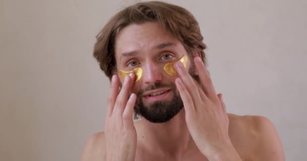 Handsome bearded man with bare torso applying golden patches under eyes for reduce black circles. Concept of treatment and cosmetology. — Stock Video