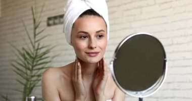 Makyajsız çekici bir kadın parlak banyodaki aynaya bakarken kendine göz kırpıyor. Kafasında havluyla mutlu esmer, doğal güzelliğinden memnun..