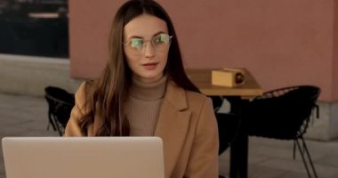 Açık havada masa başında oturan ve iş için dizüstü bilgisayarlı akıllı telefon kullanan günlük kıyafetlerle meşgul çekici bir kadın. Serbest çalışan kadın temiz havada en sevdiği işi yapıyor..