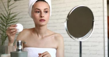 Banyo havlusundaki çekici genç kadın sabah duşundan sonra yüzünü temizlemek için pamuk pedi kullanıyor. Saf sağlıklı ten kavramı.