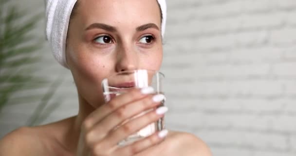 Atrakcyjna młoda brunetka pijąca wodę ze szkła siedząc w łazience. Młoda kobieta z naturalnym pięknem utrzymuje równowagę wodną. — Wideo stockowe