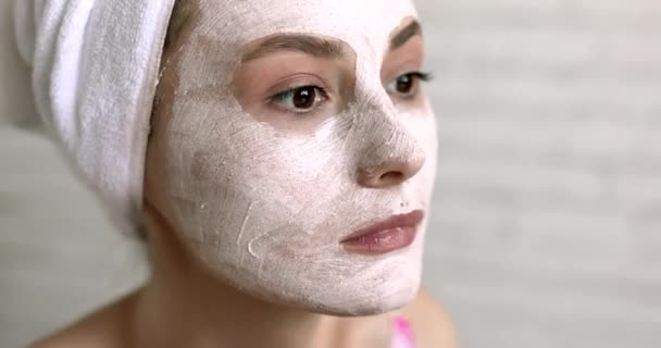 Mulher atraente em toalha de banho branco colocando máscara branca no rosto com aplicador enquanto está em pé no banheiro. Conceito de beleza e cuidados de saúde. — Vídeo de Stock