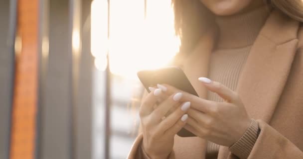 Close-up van vrouwelijke handen met trendy witte manicure met zwarte moderne smartphone. Jonge vrouw in beige jas met behulp van draadloze gadget op straat. — Stockvideo