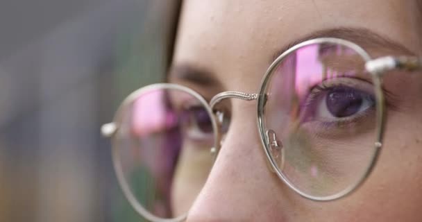 Close up of pretty young woman with clear skin wearing round eyeglasses. Reflection in lenses. Female standing outdoors and looking aside. — Stock Video