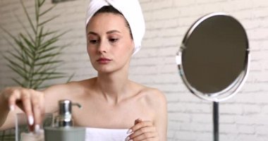 Yüzü losyonla temizlemek için pamuk pedi kullanan banyo havlusuyla çekici genç bir bayan. Mutlu kadın banyoda oturuyor ve sabah hijyen yapıyor..