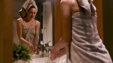 Beyaz lavaboda ellerini sabunla yıkayan terli havluyla göz kamaştırıcı genç bir bayan. Modern banyodaki aynada yansıması. Sabah rutini ve hijyen anlayışı.