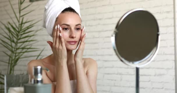 Elbűvölő fiatal hölgy, csupasz vállakkal masszírozza az arcát a reggeli zuhany után. Boldog barna néz tükör és csinál bőr ellátás rutin otthon. — Stock videók
