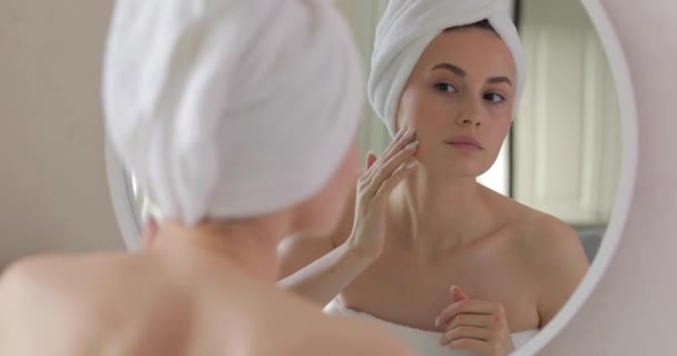 Απογοητευμένη νεαρή γυναίκα με πετσέτα μπάνιου προσπαθεί να αφαιρέσει μερικές μαύρες κηλίδες στο πρόσωπό της, ενώ κοιτάζει τον καθρέφτη. Γυναίκα κάνει διαδικασίες φροντίδας του δέρματος κατά τη διάρκεια της πρωινής ώρας. — Αρχείο Βίντεο