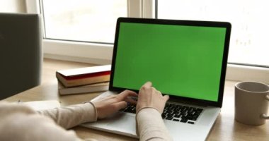 Ofiste çalışan bir iş kadınının omuz üstü fotoğrafı. Masanın üstünde, yeşil ekrana bakıyor. Ofisteki kişi dizüstü bilgisayarı kullanıyor, yeşil ekranlı, tahta masada oturuyor.