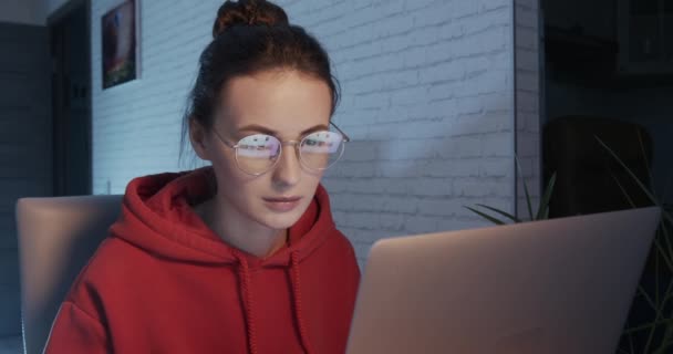 Kırmızı kapüşonlu hoş bir kadın evde dizüstü bilgisayar kullanıyor. — Stok video