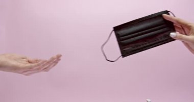 Kadın eli başka bir ele siyah tıbbi maske takıyor.