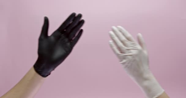 Großaufnahme von Menschen in schwarz-weißen Medizinhandschuhen, die Hände über rosa Hintergrund schütteln. Kommunikation während des Coronavirus. Schutzkonzept. — Stockvideo