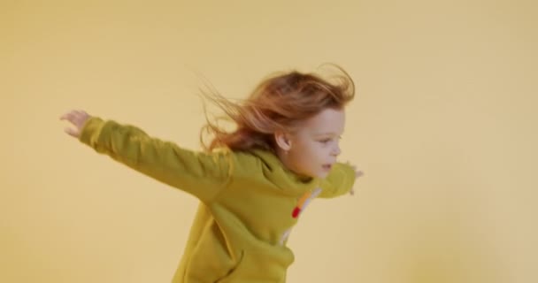 Belle enfant femelle aux cheveux blonds jouant seule en studio avec fond jaune. Enfant heureux en vêtements décontractés passer du temps à l'intérieur. — Video