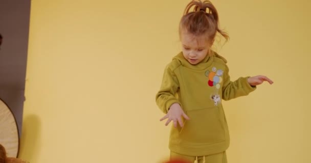 Bedårande liten unge i snygg overall leker med röd boll över gul bakgrund. Glada barn använder leksaker för att ha kul inomhus. — Stockvideo