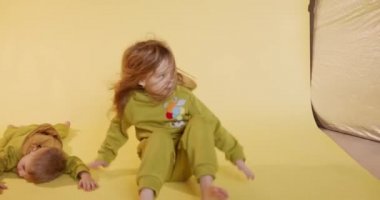 Aktif kadın çocuk yerde oturuyor ve küçük çocuk yanında dinlenirken etrafında dönüyor. İki çocuk stüdyoda eğlenerek vakit geçiriyorlar..