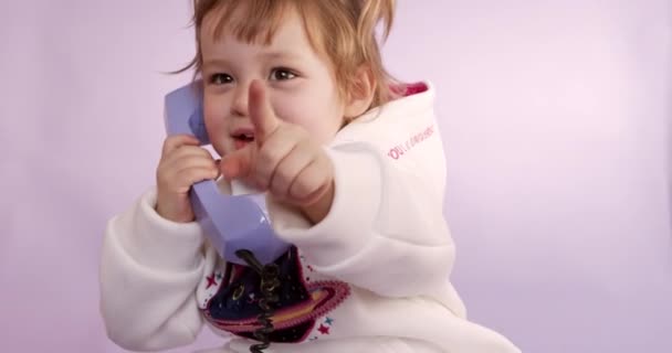 Adorable niño pequeño con dos colas de caballo cortas hablando con auriculares y gestos pasados de moda. Aislado sobre fondo de estudio rosa. Niño feliz juguetón. — Vídeo de stock