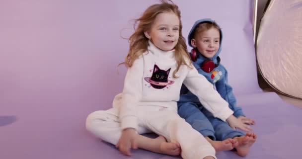 两个穿着连衣裙快乐的孩子坐在工作室的地板上，一起玩耍。友谊、童年和乐趣的概念. — 图库视频影像