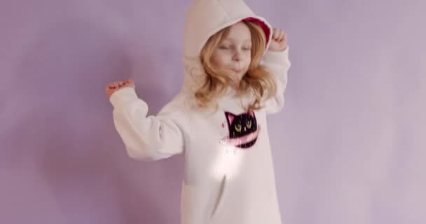 漂亮的小女孩穿着毛衣,头罩在粉色的背景上唱歌跳舞.快乐的金发碧眼的孩子在业余时间玩得很开心. — 图库视频影像