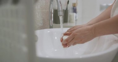Genç bir kadın musluğun altında ellerini yıkarken sabun kullanıyor. Ellerinizi köpükle kapatın. Hijyen kavramı.