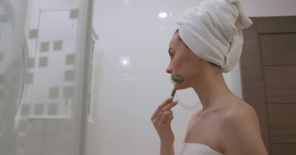 Atrakcyjna kobieta z białym ręcznikiem na głowie stojąca przed lustrem i wykonująca zabiegi pielęgnacyjne po prysznicu. Pojęcie piękna i higieny. — Wideo stockowe