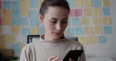 Kahverengi saçlı çekici bir kadın evde akıllı telefon kullanıyor. İşyerinde notlarla dolu renkli kağıt çubuklarla oturan serbest çalışan bir kadın..