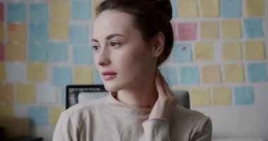 Kahverengi saçlı bitkin bir kadın dizüstü bilgisayarla çalışırken kameraya bakıyor. Bağımsızlık, teknoloji ve aşırı çalışma kavramı.