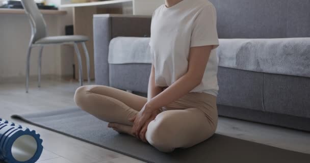 Close up de jovem mulher em roupas esportivas sentado no tapete de ioga em pose de lótus e se preparando para a meditação. Respiração feminina profunda e relaxante durante o treino em casa. — Vídeo de Stock