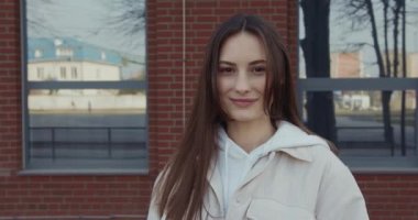 Güzel, koyu renk saçlı, şık giyinmiş, gülümseyen ve sokakta kameraya bakan hoş bir kadın. Gençlik ve yaşam tarzı kavramı.