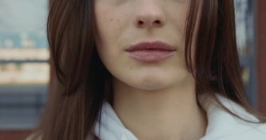 Tam burunlu ve dolgun dudaklı bir kadın yüzü. Hafif rüzgar düz kahverengi saçlar savuruyor. Kadın dışarıda duruyor..