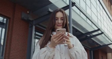 Güzel bir genç bayan boş zamanlarında modern akıllı telefon kullanıyor. Güzel esmer, şık günlük kıyafetler giyiyor. Teknoloji konsepti.