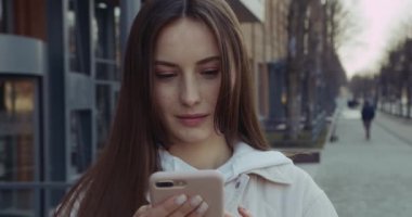 Sıradan kıyafetler giymiş, sokakta dikilip modern akıllı telefon kullanan mutlu ve çekici bir esmer. İnsan kavramı, teknoloji ve yaşam tarzı.