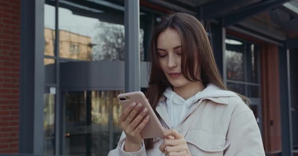 Açık havada dikilen ve modern akıllı telefon kullanan güzel mutlu kadın portresi. Güzel esmer kız, elinde kişisel aletlerle temiz havada vakit geçiriyor.. — Stok video