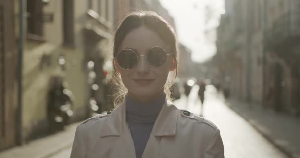 Πορτρέτο της γοητευτικής γυναίκας σε μοντέρνα στρογγυλά γυαλιά ηλίου που θέτουν σε εξωτερικούς χώρους. Αξιολάτρευτο θηλυκό με καστανά μαλλιά χαλαρώνει στον καθαρό αέρα. — Αρχείο Βίντεο