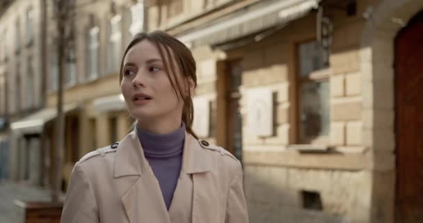 Wunderschöne junge Frau mit braunen Haaren, trendiger Sonnenbrille und Kleidung, die auf der Straße in der Nähe moderner Gebäude spaziert. Urbaner Raum. Lifestyle-Konzept. — Stockvideo