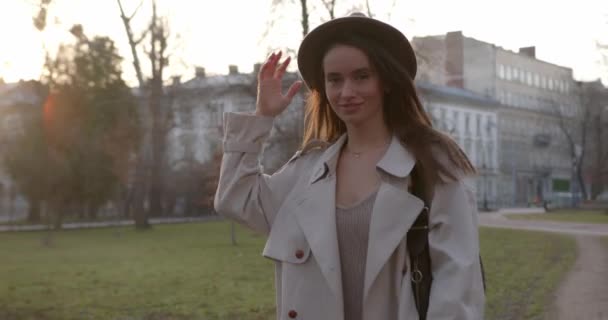 Prachtige donkerharige vrouw met trendy hoed en jas die alleen in het stadspark loopt. Concept van mens, mode en levensstijl. — Stockvideo