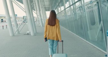 Aydınlatıcı ceketli genç bir kadın şehir merkezinde yürüyor ve modern akıllı telefon kullanıyor. İnternette iş meselelerini çözen pozitif iş kadını.