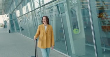 Aydınlatıcı ceketli genç bir kadın şehir merkezinde yürüyor ve modern akıllı telefon kullanıyor. İnternette iş meselelerini çözen pozitif iş kadını.